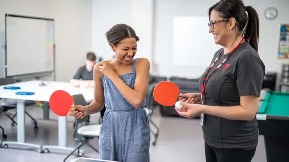 A teenager and a YMCA staff member share a laugh while playing table tennis