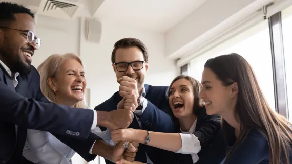 Five office workers put their hands together in a show of team unity