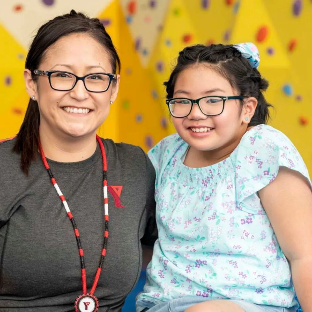 A YMCA child care worker and a preteen girl in a gymnasium, smiling