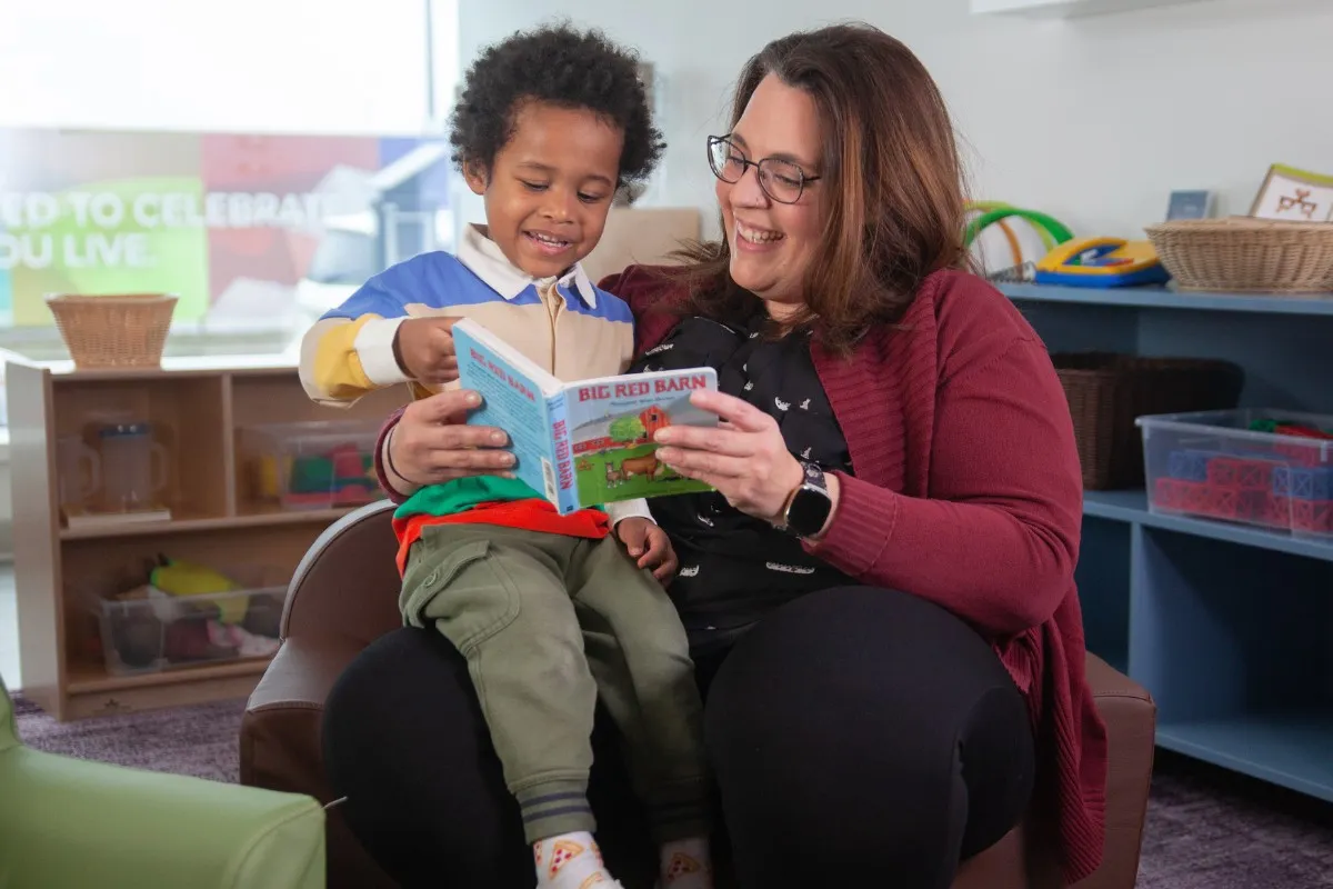 A woman reads to a young boy in her lap at a child care centre