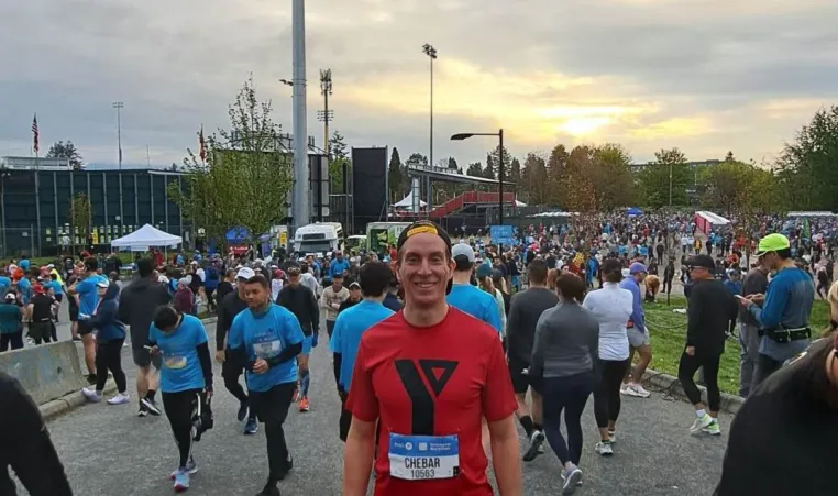 A man in a YMCA shirt and race bib among the crowd at the BMO Vancouver Marathon.