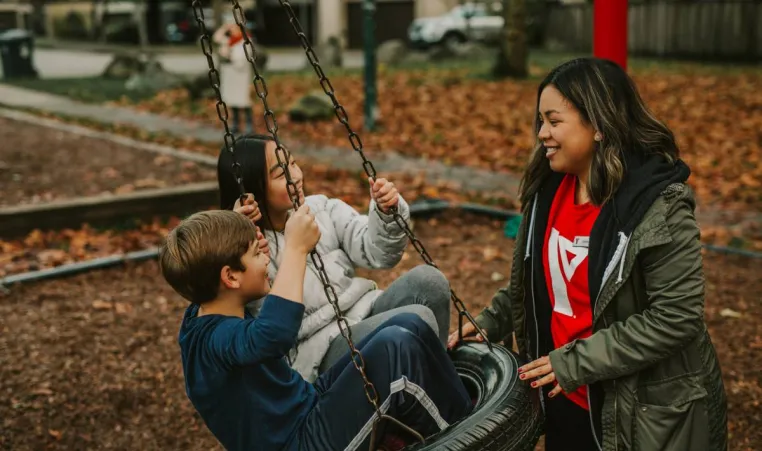 A YMCA BC child care staff member pushing two children on a tire swing